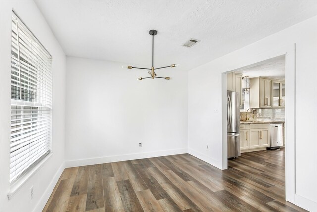 unfurnished dining area with an inviting chandelier, sink, dark hardwood / wood-style floors, and a textured ceiling