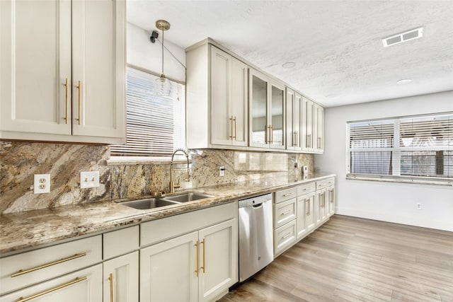 kitchen featuring sink, hanging light fixtures, light stone counters, light hardwood / wood-style floors, and stainless steel dishwasher