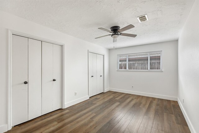 unfurnished bedroom with multiple closets, ceiling fan, dark wood-type flooring, and a textured ceiling