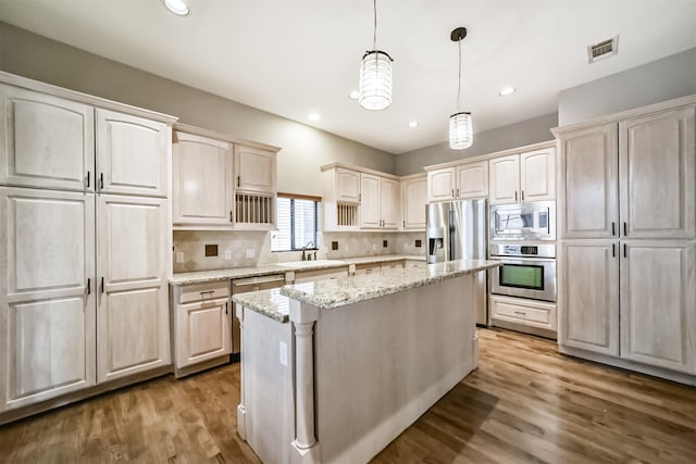 kitchen featuring pendant lighting, hardwood / wood-style flooring, stainless steel appliances, light stone counters, and a kitchen island