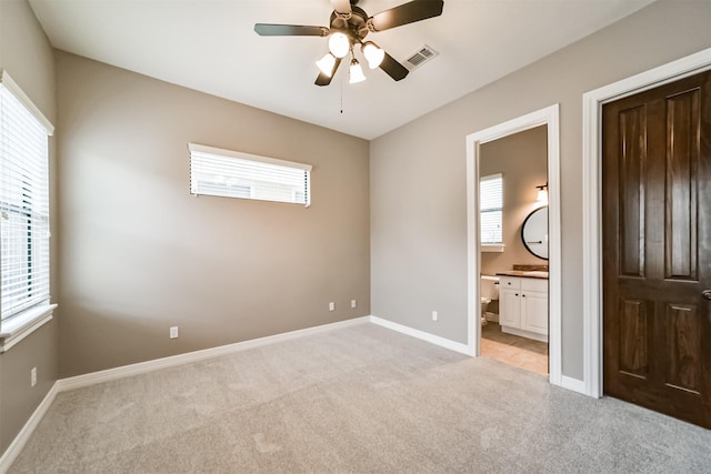 unfurnished bedroom with multiple windows, light colored carpet, ceiling fan, and ensuite bathroom