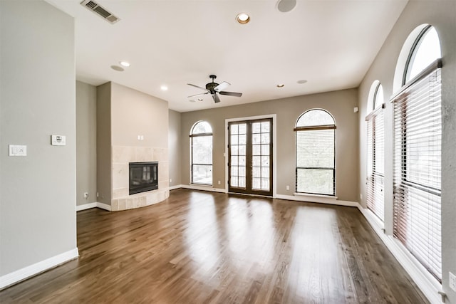 unfurnished living room with a tile fireplace, dark hardwood / wood-style floors, ceiling fan, and french doors