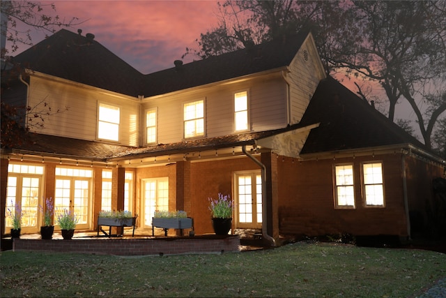 back house at dusk featuring a lawn