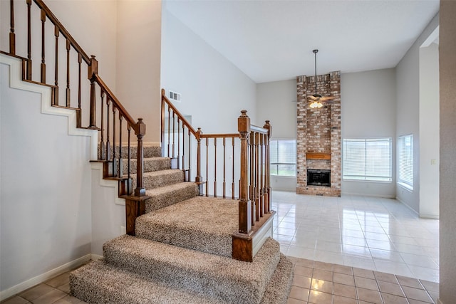 stairs with ceiling fan, tile patterned floors, a brick fireplace, and a high ceiling