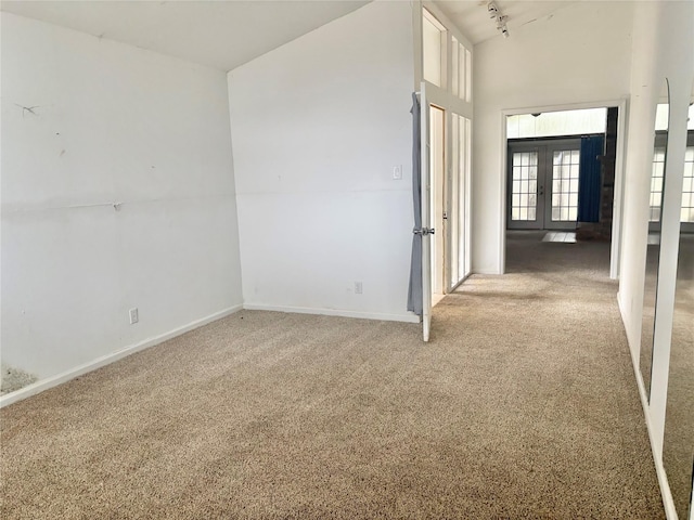 carpeted empty room with french doors, rail lighting, and high vaulted ceiling