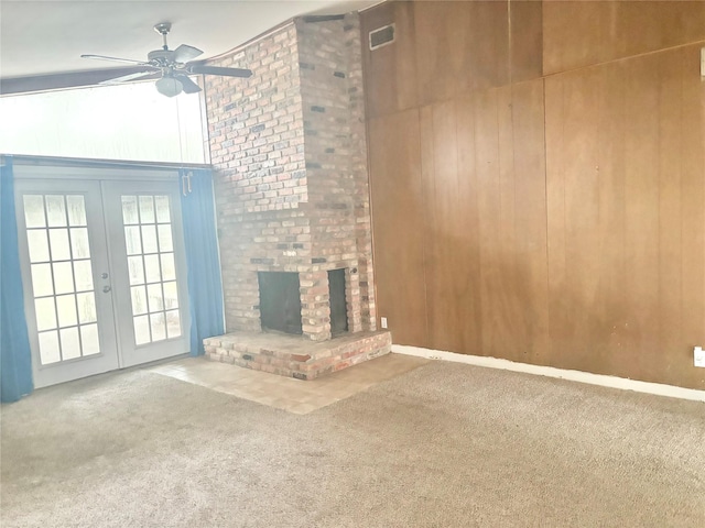 unfurnished living room with wooden walls, carpet floors, a high ceiling, ceiling fan, and a brick fireplace