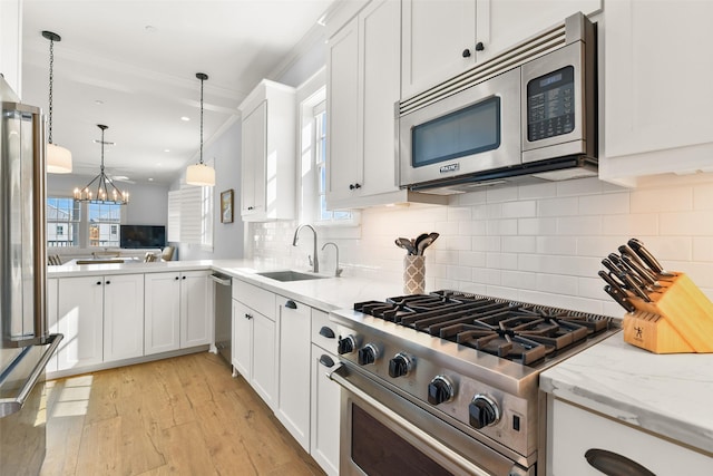 kitchen featuring pendant lighting, sink, white cabinets, stainless steel appliances, and light wood-type flooring