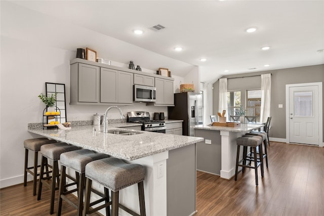 kitchen featuring appliances with stainless steel finishes, gray cabinetry, a kitchen bar, kitchen peninsula, and light stone countertops