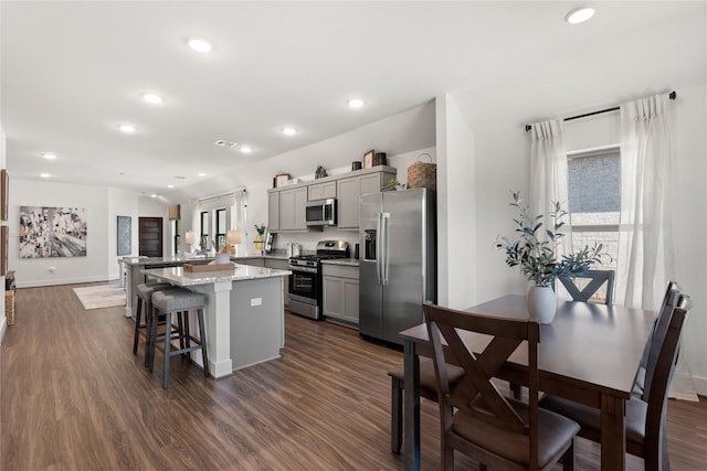 kitchen with a breakfast bar area, appliances with stainless steel finishes, gray cabinetry, a center island, and light stone counters