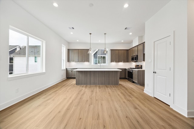 kitchen with a kitchen island, hanging light fixtures, stainless steel appliances, a healthy amount of sunlight, and light hardwood / wood-style flooring