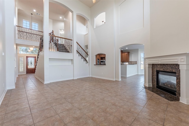 unfurnished living room with a high end fireplace, plenty of natural light, light tile patterned flooring, and a high ceiling