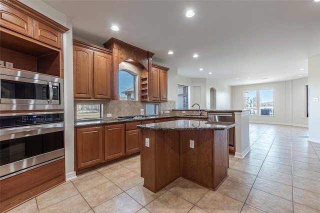 kitchen featuring sink, appliances with stainless steel finishes, backsplash, a kitchen island, and dark stone counters