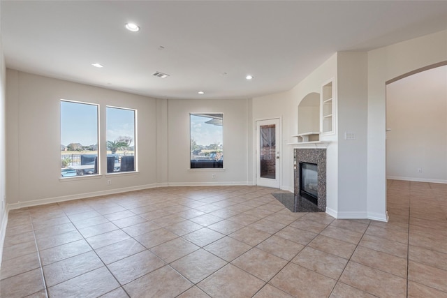 unfurnished living room with a premium fireplace, built in features, and light tile patterned floors