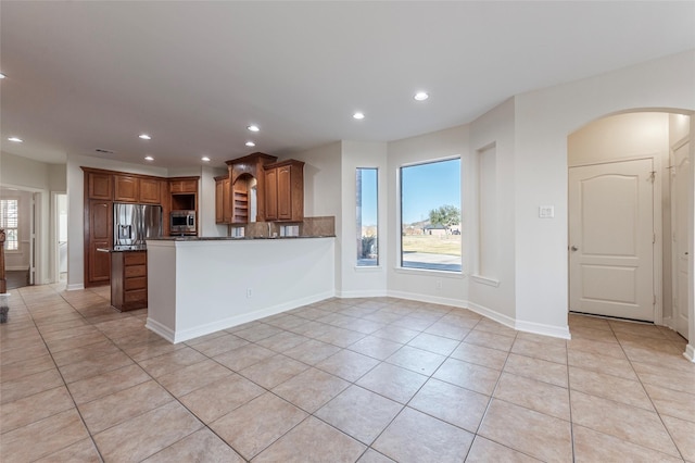 kitchen featuring stainless steel appliances, kitchen peninsula, dark stone counters, and light tile patterned flooring