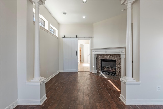 unfurnished living room featuring dark wood-type flooring, decorative columns, a barn door, and a tile fireplace