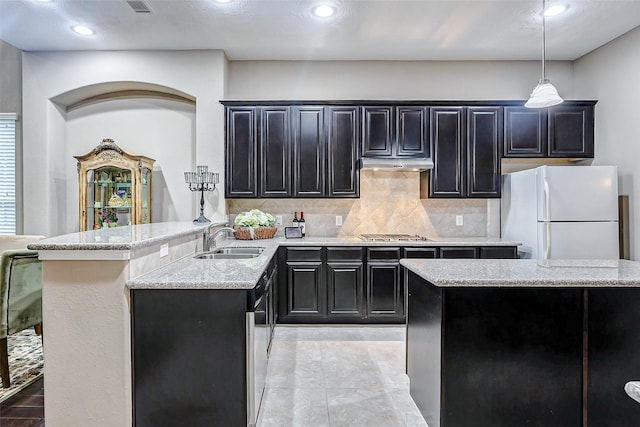 kitchen featuring decorative light fixtures, stainless steel gas stovetop, sink, decorative backsplash, and white fridge