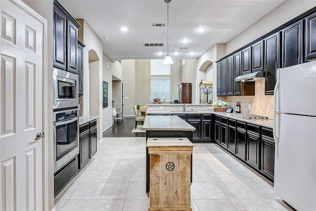 kitchen with sink, stainless steel appliances, a center island, decorative backsplash, and decorative light fixtures