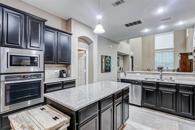 kitchen featuring sink, backsplash, a center island, light stone counters, and stainless steel appliances