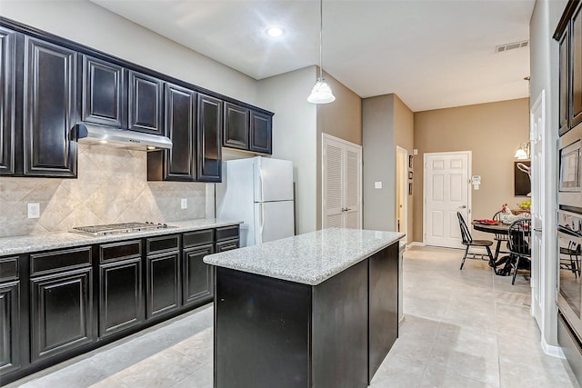 kitchen with light stone counters, decorative backsplash, a kitchen island, decorative light fixtures, and white fridge