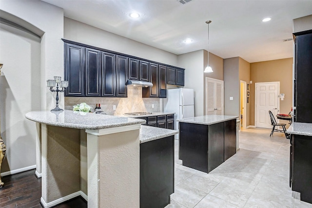 kitchen with decorative backsplash, hanging light fixtures, white refrigerator, a center island, and light stone counters