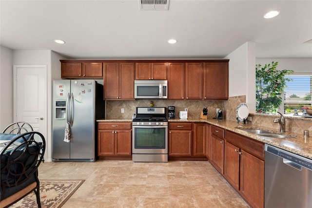 kitchen with tasteful backsplash, stainless steel appliances, light stone countertops, and sink