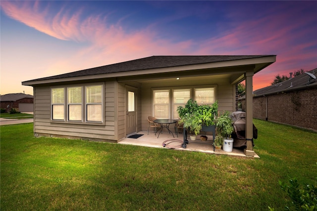 back house at dusk with a patio area and a lawn