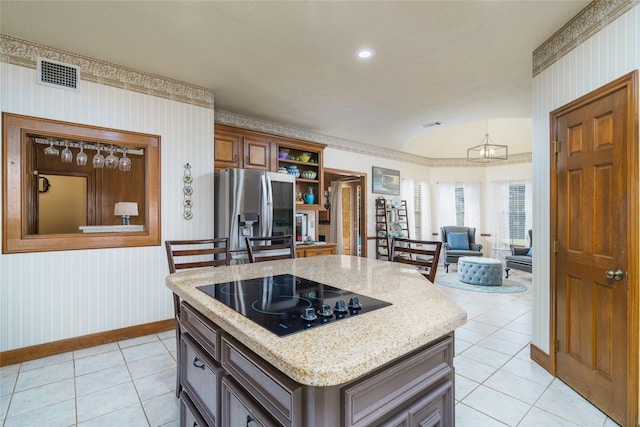 kitchen with stainless steel refrigerator, a kitchen island, black electric stovetop, light tile patterned flooring, and vaulted ceiling