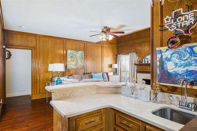 kitchen featuring dark wood-type flooring, sink, wooden walls, kitchen peninsula, and ceiling fan