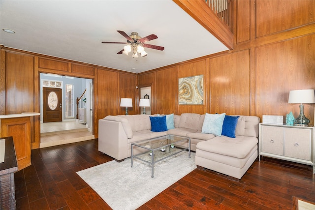 living room featuring dark wood-type flooring, ceiling fan, and wood walls