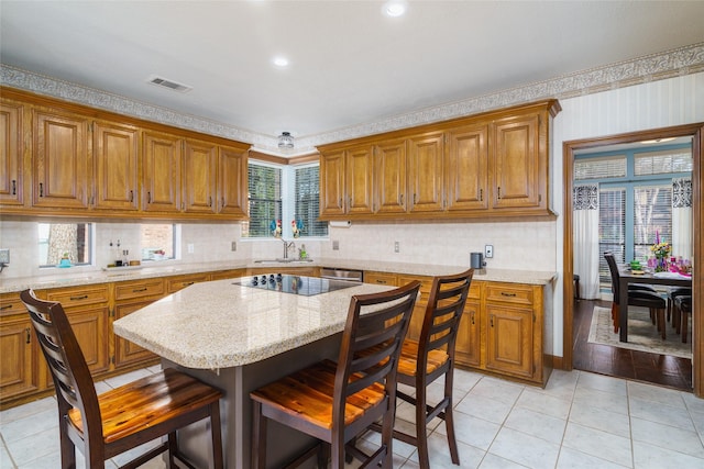 kitchen with light tile patterned floors, backsplash, a kitchen breakfast bar, a center island, and light stone counters