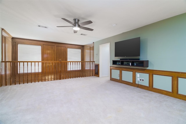 unfurnished living room featuring light colored carpet, ceiling fan, and wood walls