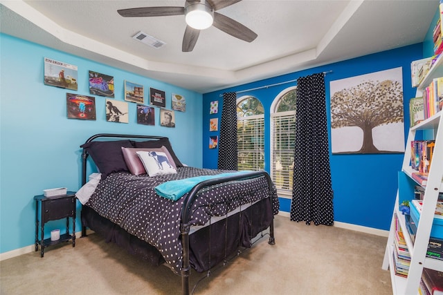 carpeted bedroom with ceiling fan and a tray ceiling