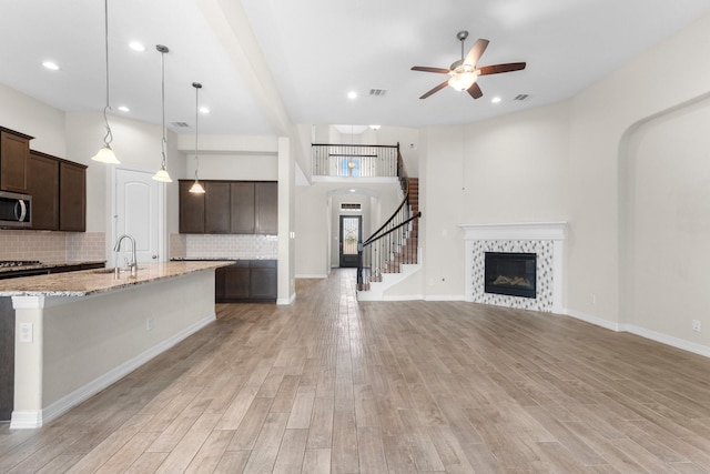 kitchen with sink, light stone counters, hanging light fixtures, dark brown cabinets, and light wood-type flooring