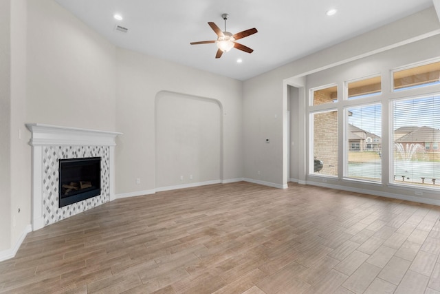 unfurnished living room with a tile fireplace, ceiling fan, and light hardwood / wood-style flooring