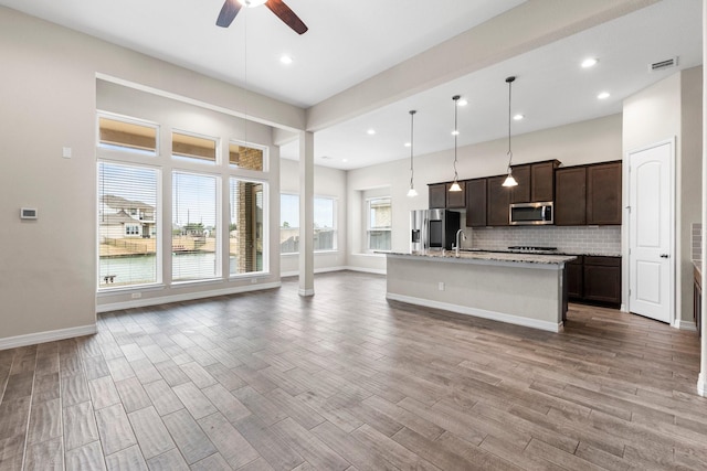 kitchen featuring appliances with stainless steel finishes, pendant lighting, an island with sink, decorative backsplash, and light wood-type flooring