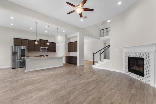 unfurnished living room featuring a towering ceiling, light hardwood / wood-style flooring, a tile fireplace, and ceiling fan