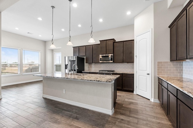 kitchen featuring stainless steel appliances, an island with sink, dark brown cabinets, and pendant lighting