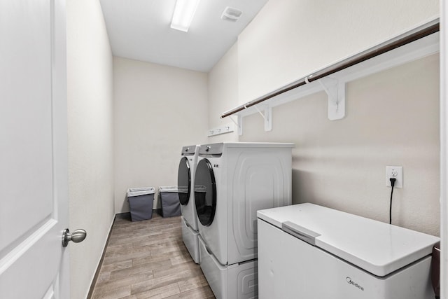 clothes washing area with washer and clothes dryer and light hardwood / wood-style floors