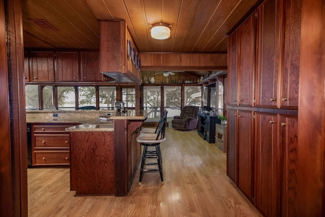 kitchen featuring a breakfast bar, wood walls, wood ceiling, and light wood-type flooring