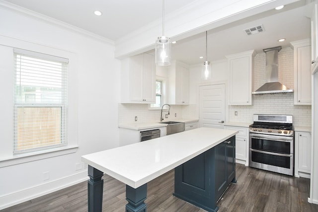 kitchen with white cabinetry, sink, hanging light fixtures, stainless steel appliances, and wall chimney range hood