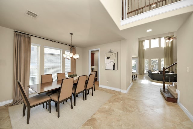 tiled dining room featuring ceiling fan with notable chandelier and a high ceiling