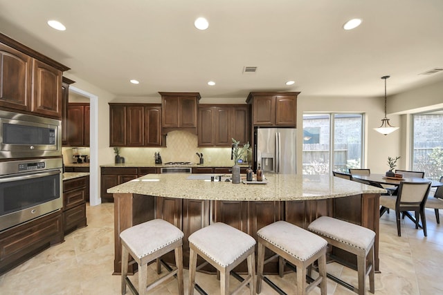 kitchen featuring a kitchen island with sink, pendant lighting, dark brown cabinets, and stainless steel appliances