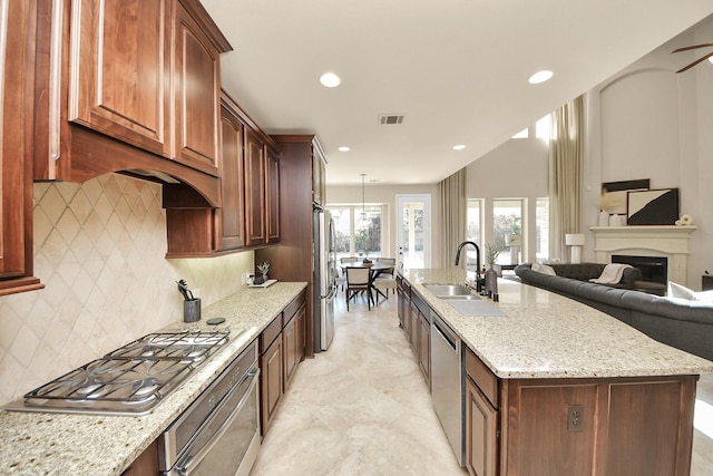 kitchen with appliances with stainless steel finishes, sink, decorative backsplash, light stone countertops, and a center island with sink