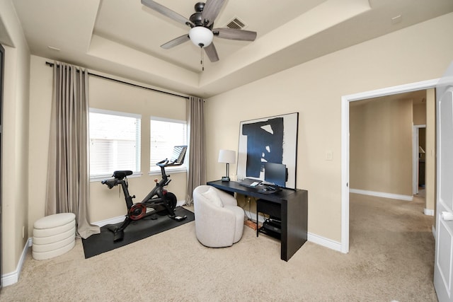 carpeted office with ceiling fan and a raised ceiling