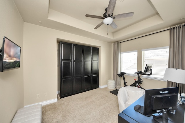 workout area featuring ceiling fan, a tray ceiling, and light carpet