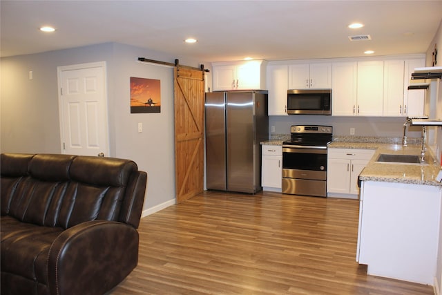 kitchen featuring appliances with stainless steel finishes, white cabinetry, sink, light stone counters, and a barn door