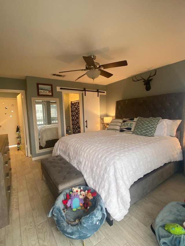 bedroom with a closet, light hardwood / wood-style flooring, a barn door, and ceiling fan