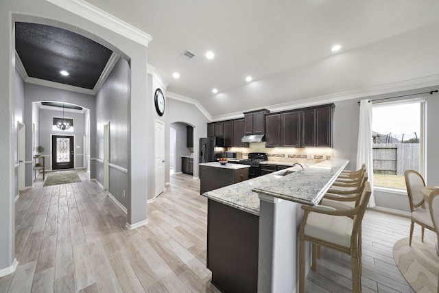 kitchen with dark brown cabinetry, a breakfast bar, light stone counters, light wood-type flooring, and black appliances