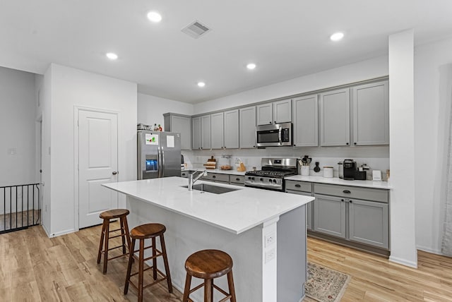 kitchen with sink, a breakfast bar area, gray cabinetry, stainless steel appliances, and a center island with sink