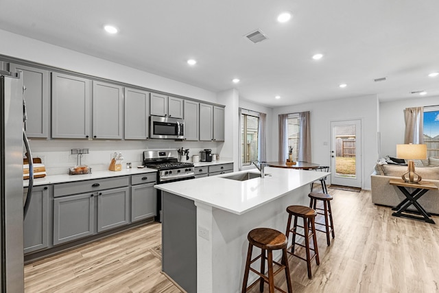 kitchen featuring stainless steel appliances, gray cabinets, a breakfast bar area, and a center island with sink